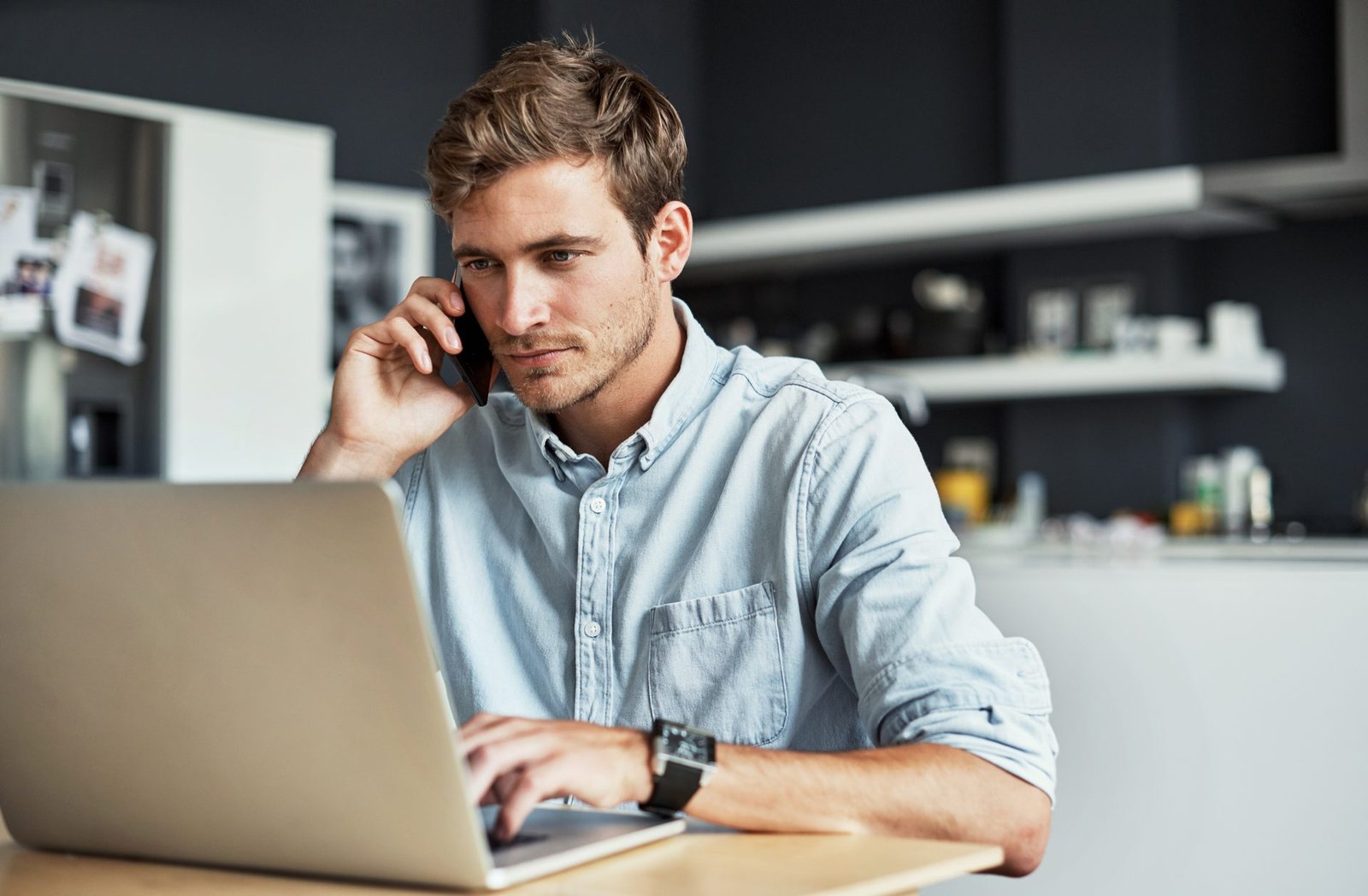 Shot of a digital marketer talking on his cellphone while using his laptop at home to complete his digital marketing services